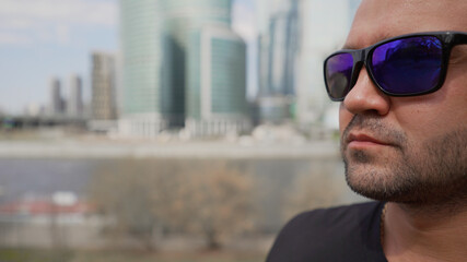 Portrait of brutal man in sunglasses in the city on the background of large building. Brutal guy in sunglasses on the background of the city. Brutal guy on the background of buildings in Moscow.