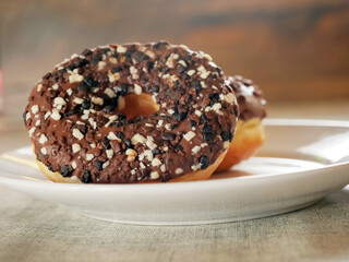 Doughnut with chocolate icing on a white plate. Pastry product. Delicious and unhealthy choice of desert. Selective focus