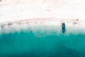 Aerial view of traditional longtail boat floating on a turquoise and clear ocean in Thailand.