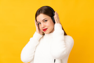Teenager girl isolated on yellow background listening music