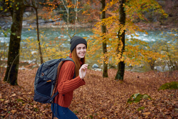 woman in a sweater with a backpack on her back near the river in the mountains and park trees autumn landscape