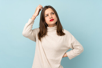 Teenager girl isolated on blue background having doubts and with confuse face expression