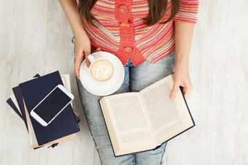 Obraz premium Close up Women Hands Holding Coffee Cup and Reading opened Book. Top view of Woman with Teacup having Break. Sitting Young Girl Study Books