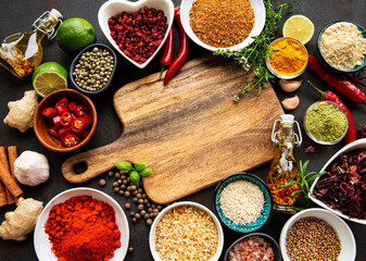 Various spices in a bowls and empty cutting board on black concrete background. Top view copy space.