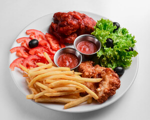 Roasted chicken wings and French fries isolated over white background. Served with fresh lettuce salad