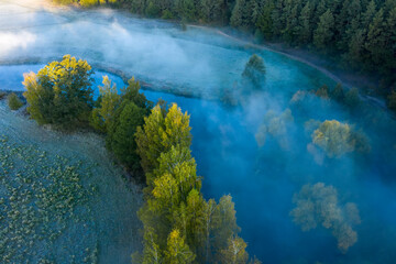 Early morning above misty river and forest. Aerial view of spring landscape of forest and river. Colorful scenery. Sunbeams on top trees. 