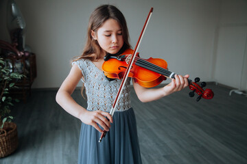 Little brunette girl in a beautiful dress playing violin indoors. Music instruments concept.