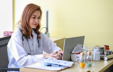 Close up of asian female doctor wearing white medical gown with stethoscope sitting at desk in hospital and concentrating on typing a prescription for patients. Healthcare, medicine concept.