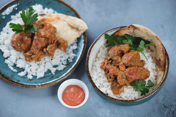 Indian chicken butter masala with white rice and flatbread, elevated view on a grey concrete background, horizontal shot