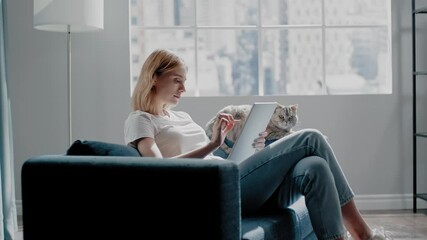 Lady works on tablet near fluffy cat sitting on blue couch