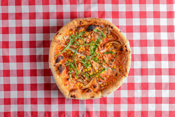 Delicious italian pizzas served on wooden table with red plaid table cloth.
