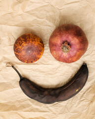Ugly food. Spoiled fruit. Rotten banana, tangerine and pomegranate lie on crumpled brown paper. Top view.