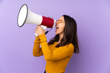 Young mixed race woman isolated on purple background shouting through a megaphone