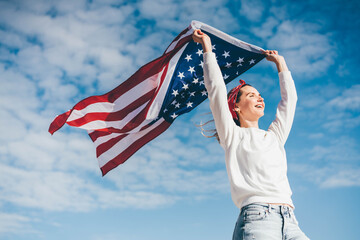 Happy woman holding united states flag against blue sky, independence day concept.