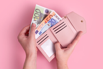 Hands holding wallet. Pink leather wallet with euro money in female hands. Closeup on a woman's hands taking European bank notes out of purse and counting. Concept of money, finances, shopping, cash.