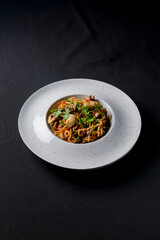 Sea food wok stir fry served in a white plate. Clams and shrimps wok isolated on black.