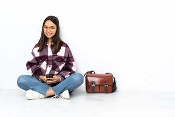 Young student woman sitting on the floor sending a message with the mobile