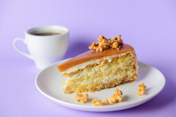 One piece of Caramel cake with pop corn on top served on a white plate. Over pastel violet purple background.