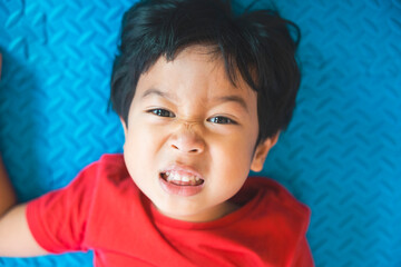 Close-up portrait Asian kids, Caucasian boy little child sleeping wearing a Red t-shirt smiling and making a funny face at the camera on blue floor background