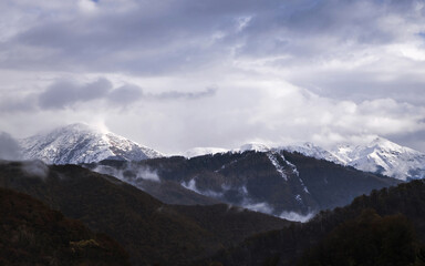 Snow peaks of the mountains and cloudy sky on the background. Beautiful scenery, outdoor snowy view. Green hills.