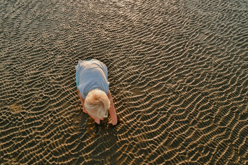 Beautiful toddler boy playing on the beach at sunset with the golden sun setting behind him. Family holiday in Queensland, Australia