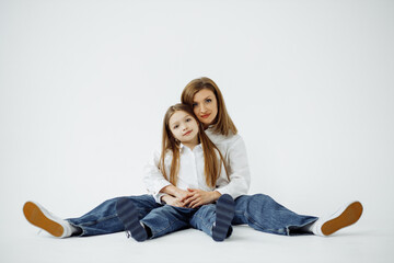 Mom with daughter sitting on the floor on a white background. Warm spring hugs, mother's day.