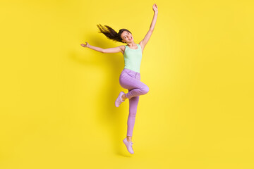 Fototapeta na wymiar Photo of charming positive lady raise hands jump wear green top pants footwear isolated yellow color background