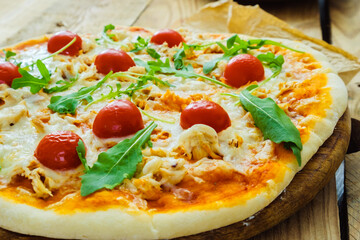 Round pizza with cheese and tomatoes on a wooden table, green basil leaves.