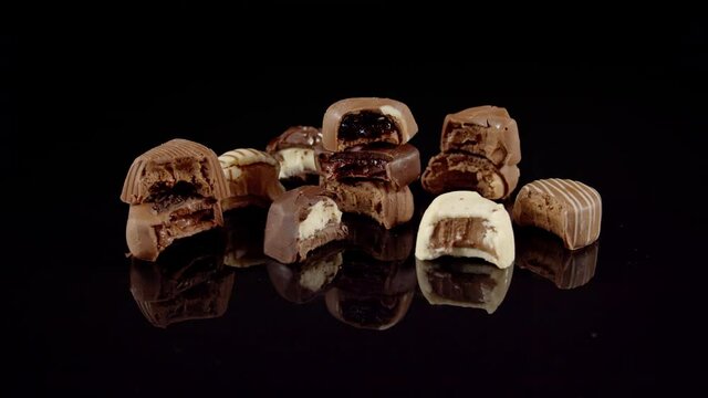 Leftover bitten chocolates pralines rotating, decorative sweets spinning after birthday holiday celebration. Bitten chocolates placed on reflective floor.