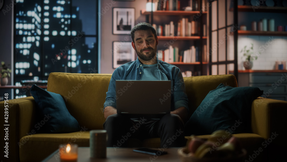 Aufkleber handsome caucasian man working on laptop computer while sitting on a sofa in dark cozy living room i