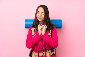 Young mountaineer girl with a big backpack over isolated pink background scheming something