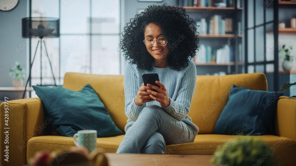 Poster portrait of a beautiful authentic latina female in a stylish cozy living room using smartphone at ho