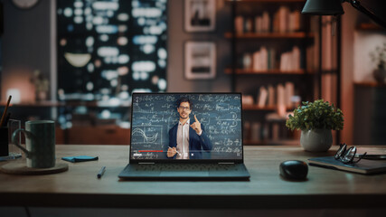 Shot of a Laptop Computer Showing Online Lecture with Portrait of a Cute Male Teacher Explaining Math Formulas. It is Standing on the Wooden Desk in Stylish Modern Home Office Studio in the Evening