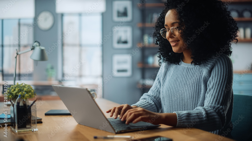Poster beautiful authentic latina female sitting at a desk in a cozy living room and using laptop computer 