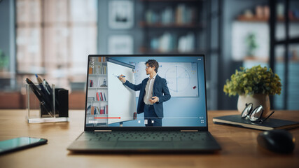 Shot of a Laptop Computer Showing Online Lecture with Portrait of a Cute Male Teacher Explaining Math Formulas. It is Standing on the Wooden Desk in Stylish Modern Home Office Studio During Day. - obrazy, fototapety, plakaty