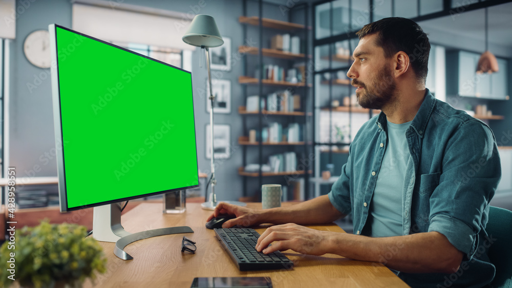 Poster handsome caucasian specialist working on desktop computer with green screen mock up display at home 