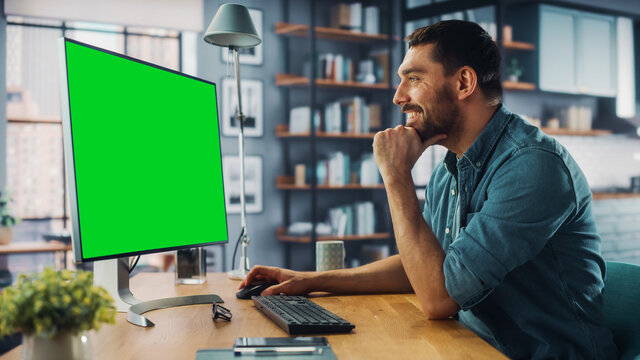 Handsome Caucasian Specialist Working on Desktop Computer with Green Screen Mock Up Display at Home Living Room. Freelance Man Chatting to Clients Over the Internet on Social Networks.