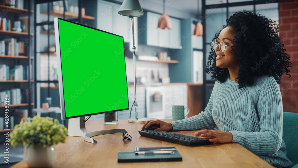 Poster latina female specialist working on desktop computer with green screen mock up display at home livin