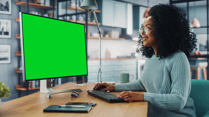 Latina Female Specialist Working on Desktop Computer with Green Screen Mock Up Display at Home...
