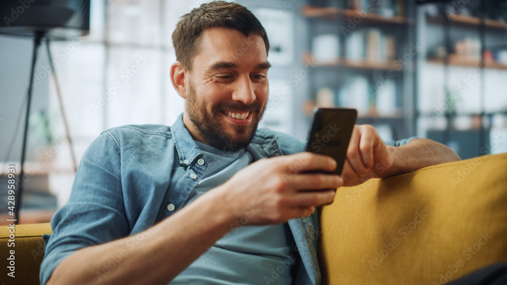 Aufkleber happy handsome caucasian man using smartphone in cozy living room at home. man resting on comfortabl