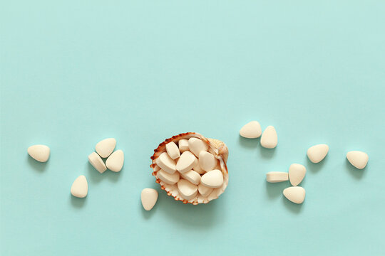 white vitamins pills in a sea shell on a blue background, healthy lifestyle concept banner with copy space on top, white tablet triangular shape