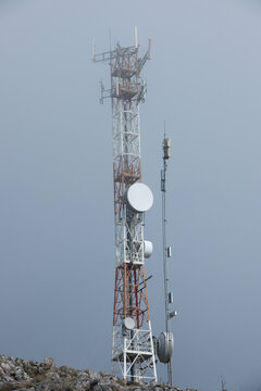 Ground view of telecommunication towers in the clouds on a mountain peak.