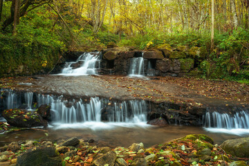 Obraz na płótnie Canvas Waterfall flowing through rocks in a deep forest, autumn landscape