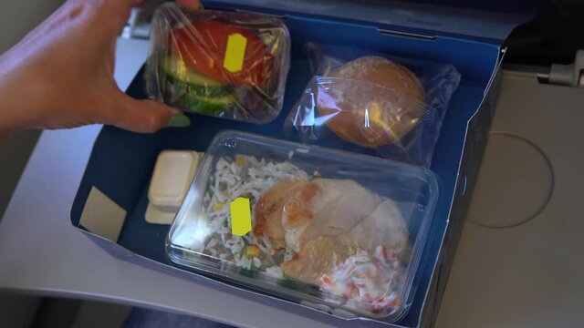 Closeup view 4k stock video footage of woman eating food on board of the flying plane. A paper box full of plastic trays with different food: rice, chicken, salad, cucumbers, tomatos, bun and butter p