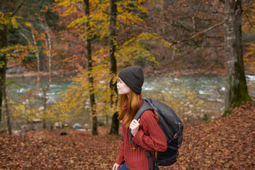 side view of happy woman in park in autumn near river and backpack on her back