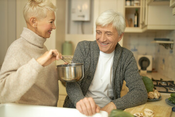 Happy retired couple cooking healthy meal in kitchen. Cheerful attractive middle aged woman...