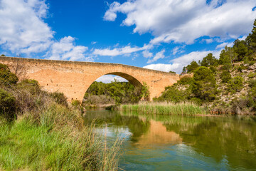 Fototapeta na wymiar Antique one arch stone bridge over a river the Hoces del Rio Cabriel Natural Park between Valencia and Cuenca in Spain. Protected Area. 