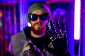 young man in glasses metallic robot hand showing gesture hi in neon lights
