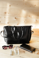 black rectangular leather bag with a rectangular leather wallet and sunglasses on a wooden table in the room. sunny day