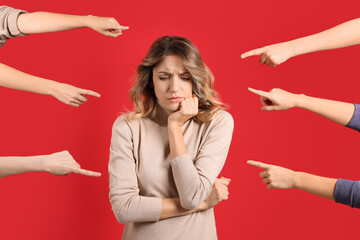 Stressed woman feeling uncomfortable because of people pointing at her against red background....